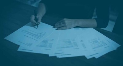 Person signing multiple advance subscription agreement documents on a dark wooden table, symbolising SEIS EIS investment paperwork
