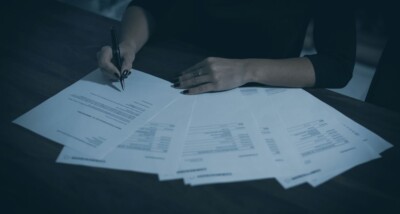 Person signing multiple advance subscription agreement documents on a dark wooden table, symbolising SEIS EIS investment paperwork