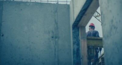 Construction worker in a red hard hat standing on a building site framed by unfinished concrete walls, illustrating an article about not being paid on a construction project and using adjudication to recover payment.