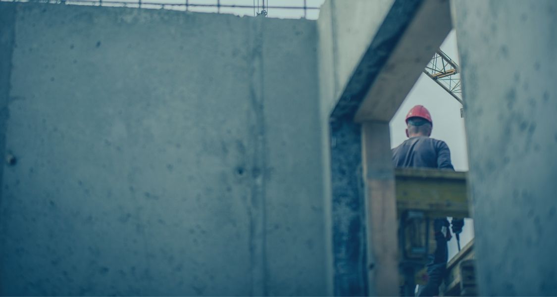 Construction worker in a red hard hat standing on a building site framed by unfinished concrete walls, illustrating an article about not being paid on a construction project and using adjudication to recover payment.