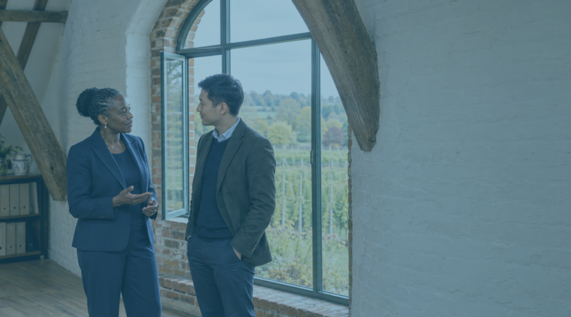 Company director and adviser discussing a transaction at an undervalue beside an arched window in a converted Kent oast-house office.