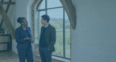 Company director and adviser discussing a transaction at an undervalue beside an arched window in a converted Kent oast-house office.