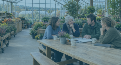 A mother and her three adult children discussing a family business demerger around a pine table in their Worcestershire garden centers' glasshouse cafe.