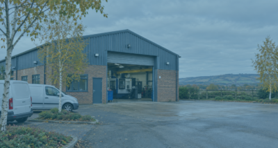 Separating commercial property - brick-and-steel engineering workshop on a Sussex business park, with open roller shutters, parked vans and autumn trees.