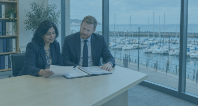 Company director and solicitor reviewing documents relating to misfeasance proceedings in a meeting room overlooking Eastbourne marina.