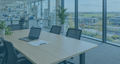 Life sciences office near Cambridge, with a laptop and printed agreement ready for reviewing ai supplier terms, overlooking a laboratory and green fields.